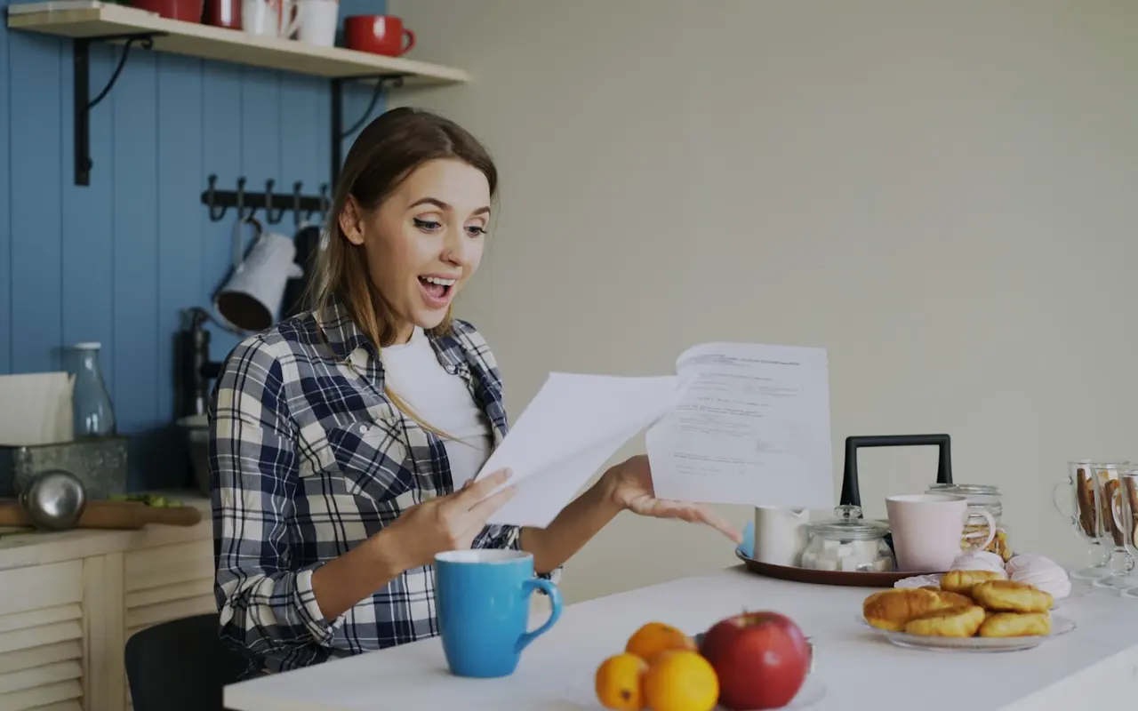 A woman delighted while reading a letter at her kitchen table