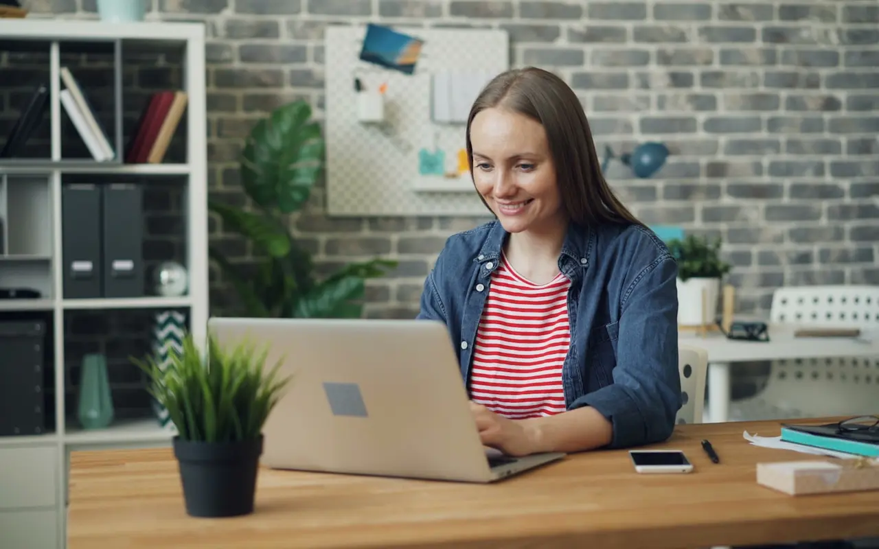 A woman smiling while typing on her laptop in a loft