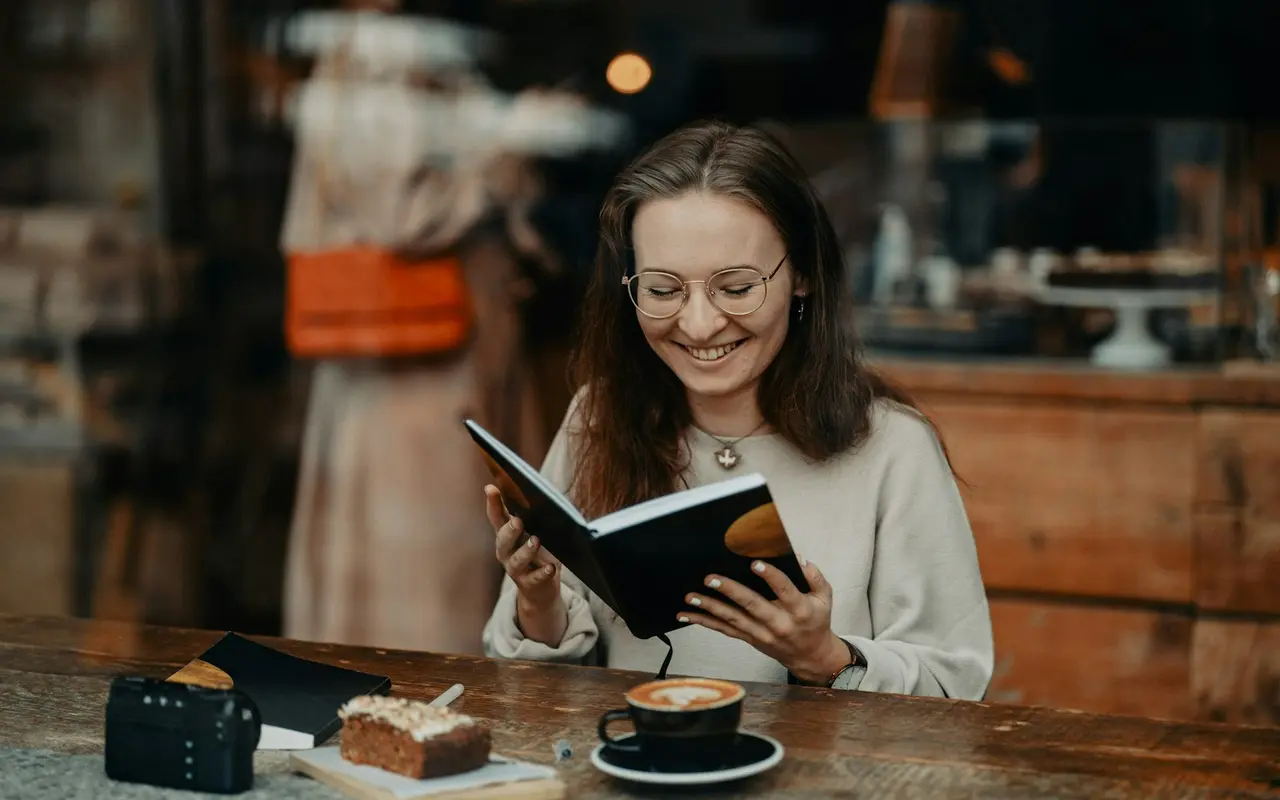 A woman reading and journaling in a warm, rustic cafe