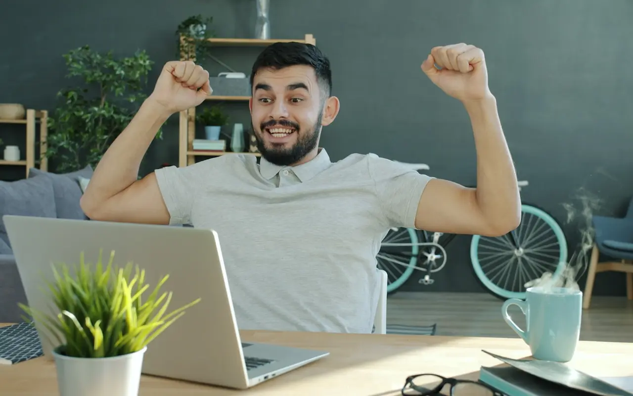 A student celebrating with a double fist-pump at his laptop