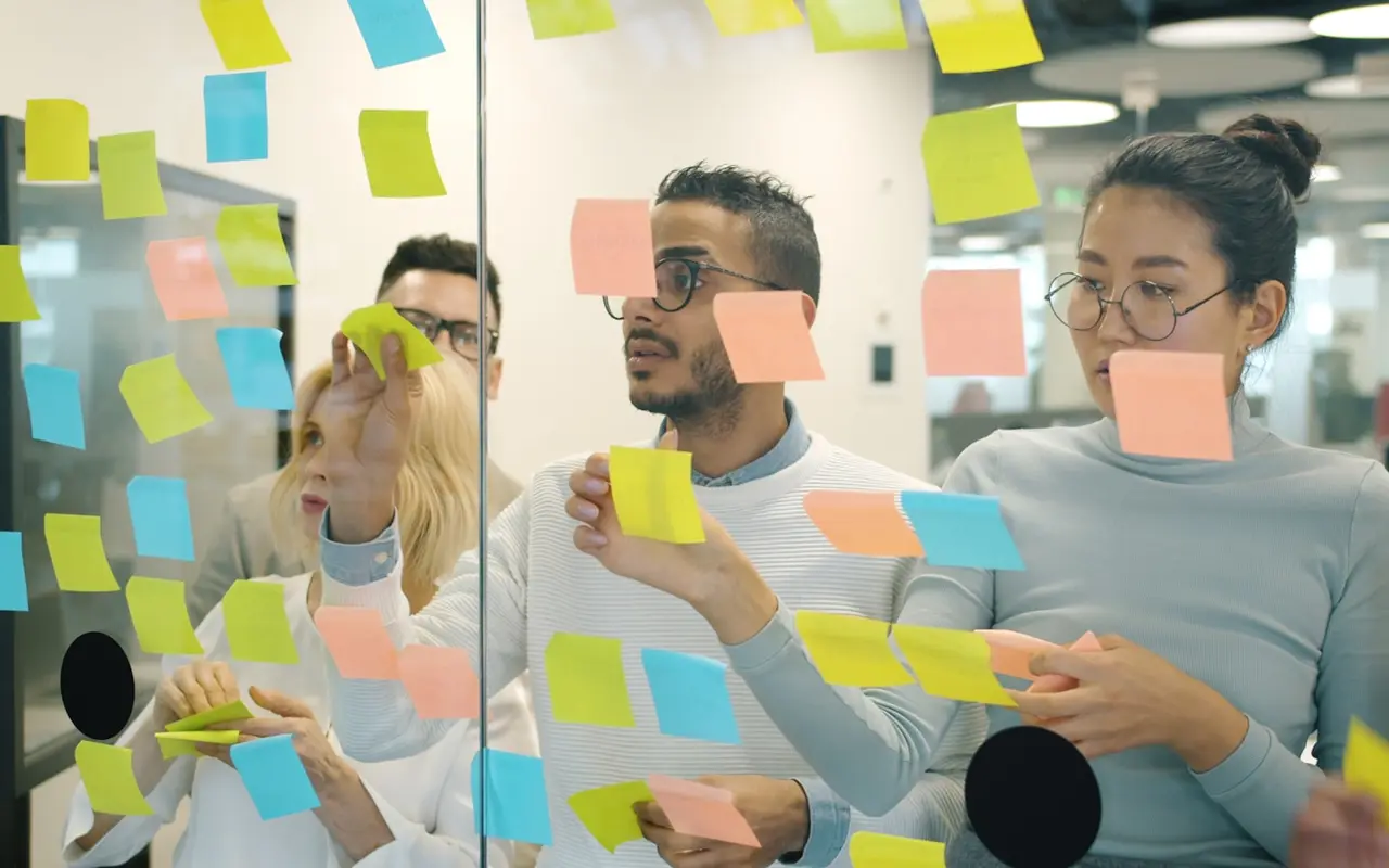Three young adults collaborating at a sticky-note covered glass wall