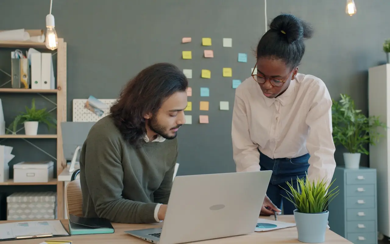 Two people reviewing research findings together over a laptop, sticky notes in soft focus